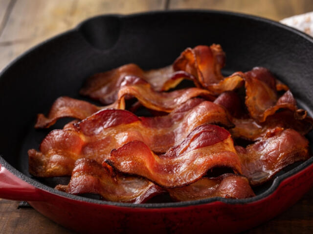 Crispy bacon slices arranged in a red cast-iron skillet on a wooden table.