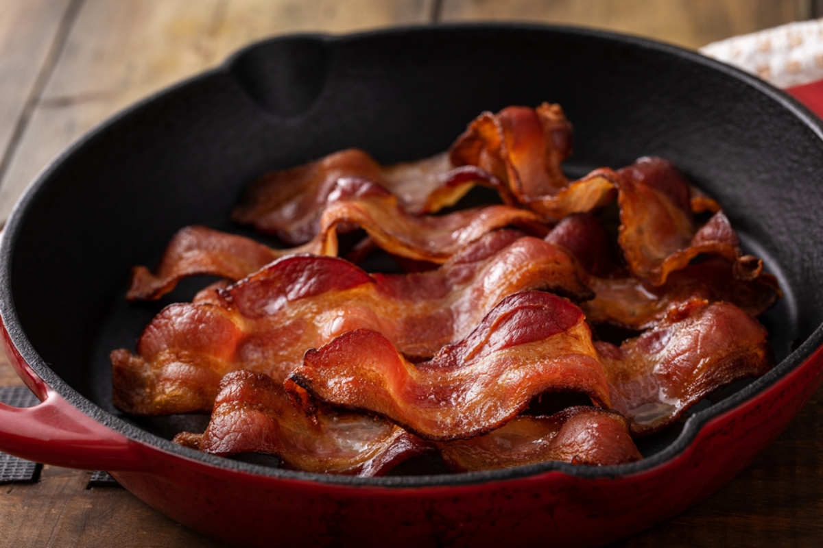 Crispy bacon slices arranged in a red cast-iron skillet on a wooden table.