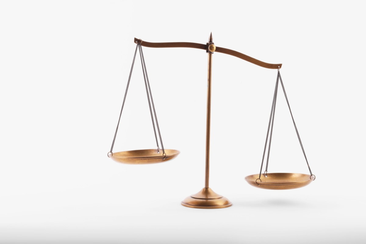 Brass balance scale with two hanging pans, symbolizing justice and fairness on a white background.