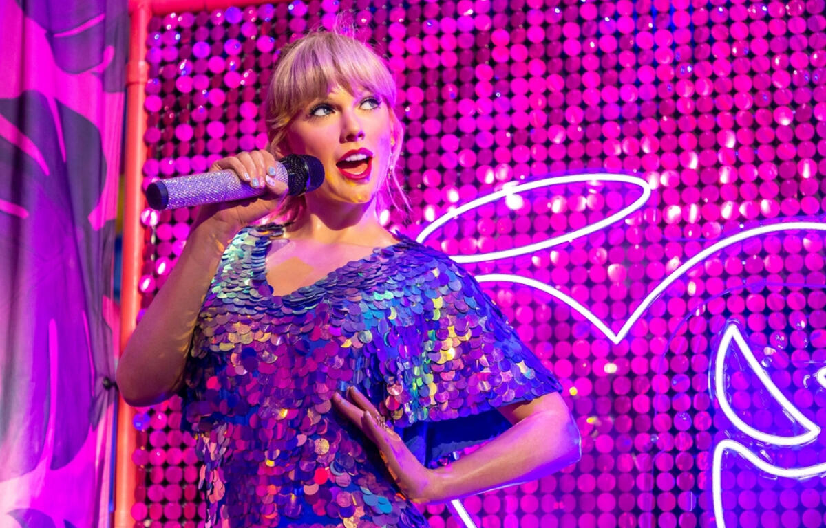 Singer performing on a colorful neon-lit stage in a sparkling blue sequined dress, holding a glittery microphone.