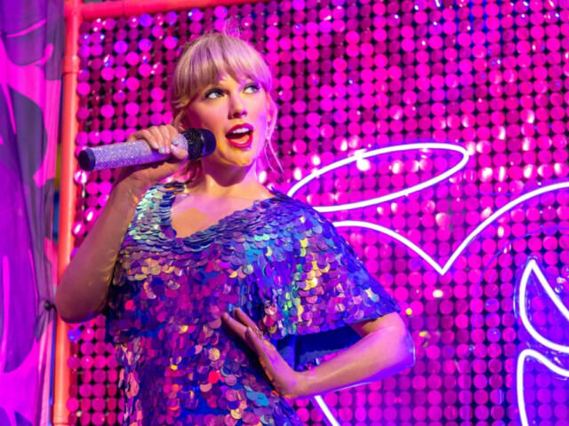 Singer performing on a colorful neon-lit stage in a sparkling blue sequined dress, holding a glittery microphone.