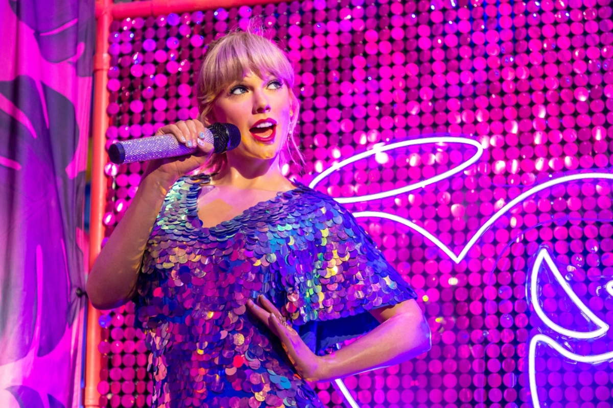 Singer performing on a colorful neon-lit stage in a sparkling blue sequined dress, holding a glittery microphone.