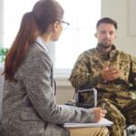 Military veteran with disability meeting with psychologist for therapy session, rehabilitation and PTSD symptoms healing. Therapist counseling soldier in wheelchair, listening, writing notes