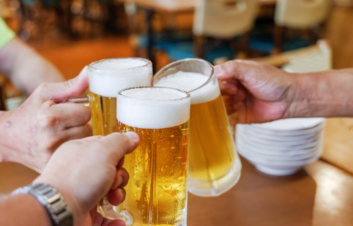 Friends raising beer mugs in a toast at a bar or restaurant, foam on top and warm lighting in the background.