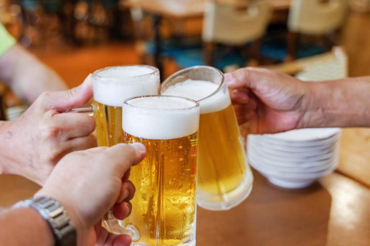 Friends raising beer mugs in a toast at a bar or restaurant, foam on top and warm lighting in the background.