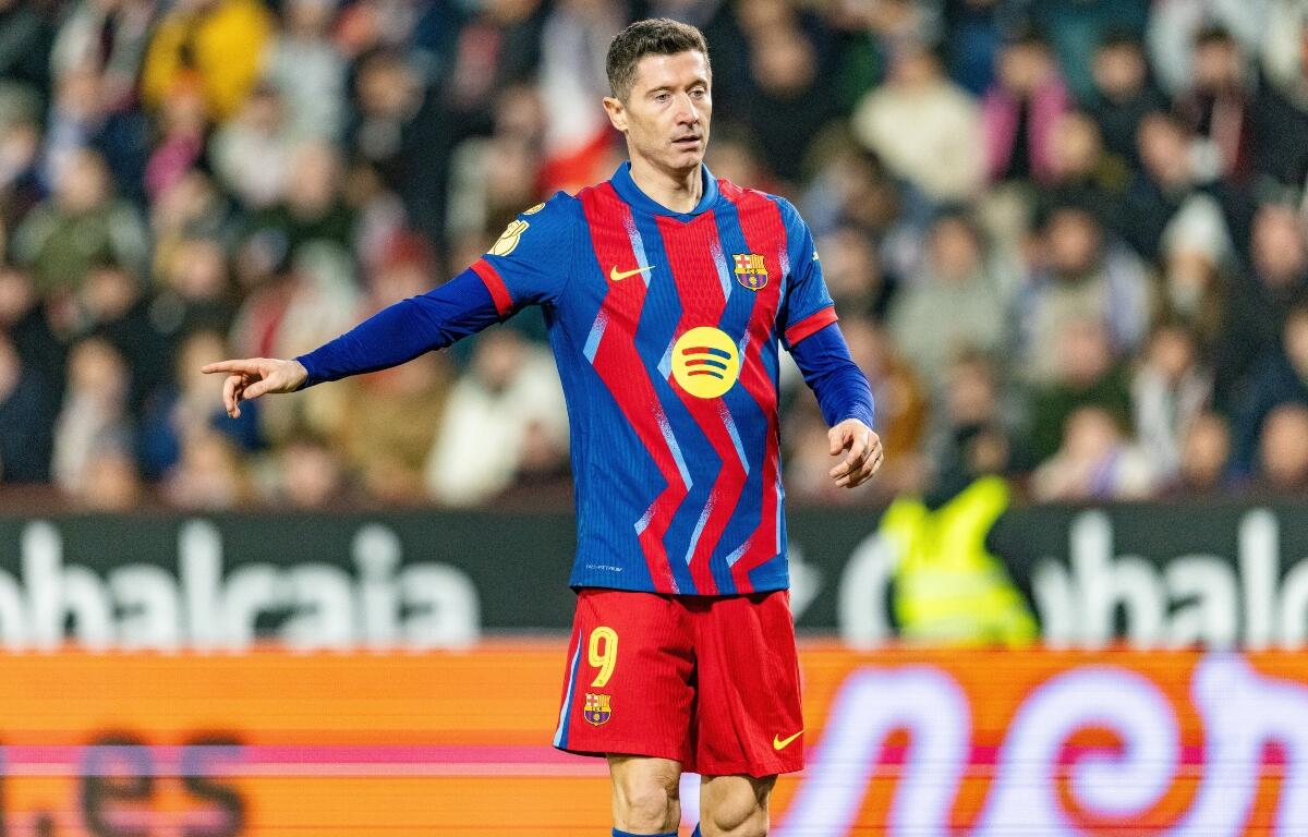 Soccer player in a blue-and-red striped Barca kit with number 9, pointing with his left arm during a match, blurred crowd in background.