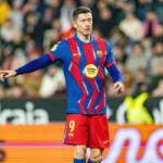 Soccer player in a blue-and-red striped Barca kit with number 9, pointing with his left arm during a match, blurred crowd in background.