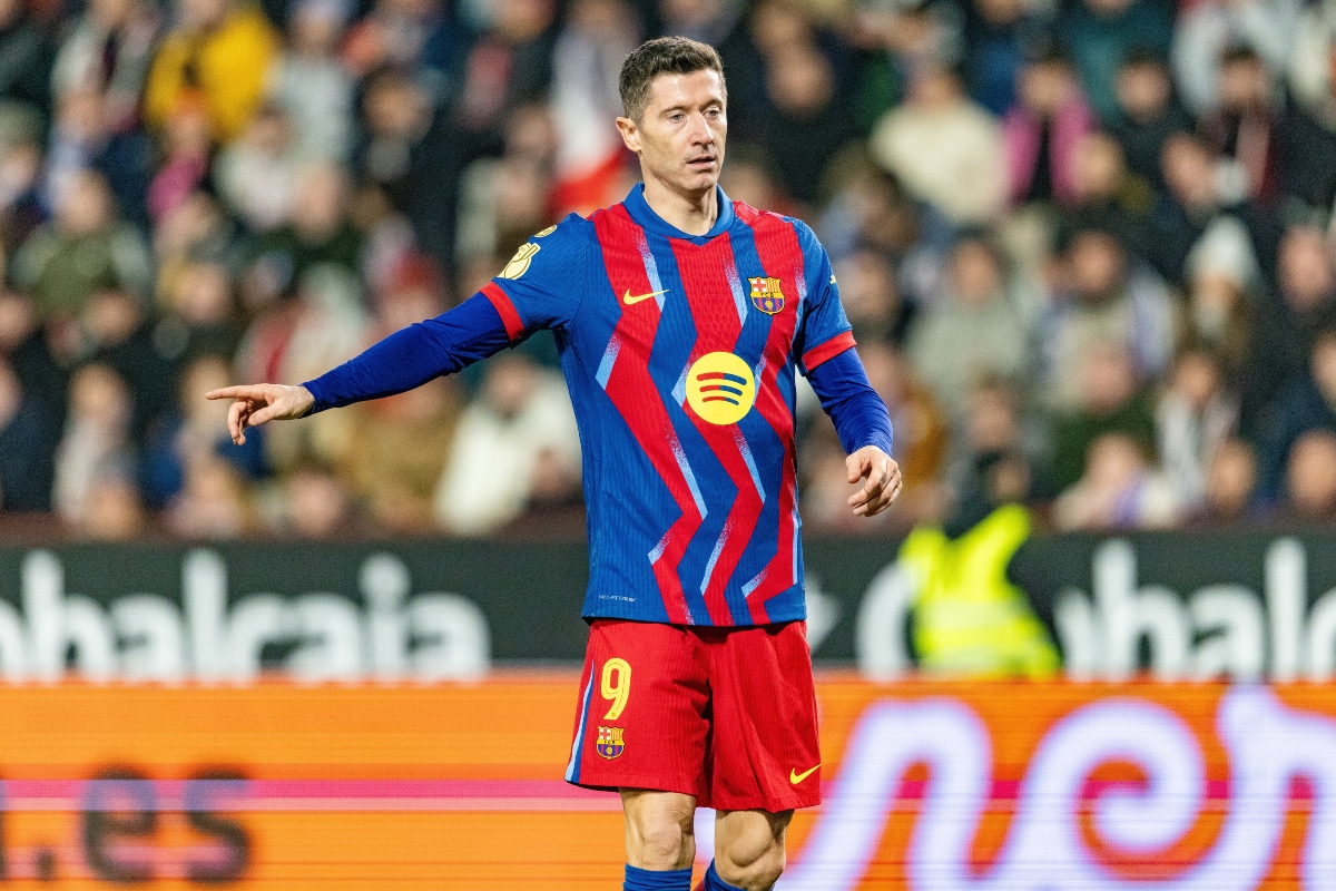 Soccer player in a blue-and-red striped Barca kit with number 9, pointing with his left arm during a match, blurred crowd in background.