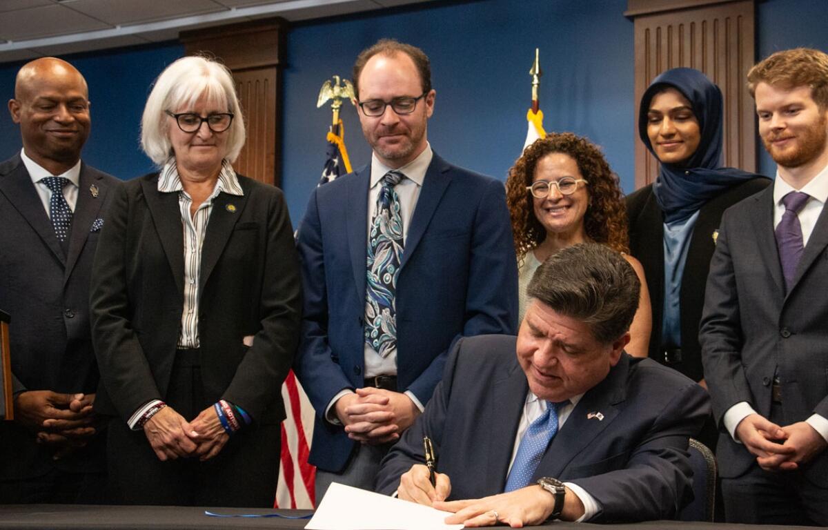 Gov. JB Pritzker signs the Artificial Intelligence Safety Measures Act into law in Chicago on July 6, 2026, surrounded by lawmakers and advocates. (Capitol News Illinois photo by Maggie Dougherty)