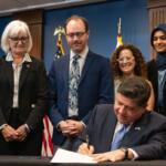 Gov. JB Pritzker signs the Artificial Intelligence Safety Measures Act into law in Chicago on July 6, 2026, surrounded by lawmakers and advocates. (Capitol News Illinois photo by Maggie Dougherty)