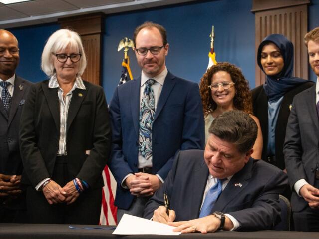 Gov. JB Pritzker signs the Artificial Intelligence Safety Measures Act into law in Chicago on July 6, 2026, surrounded by lawmakers and advocates. (Capitol News Illinois photo by Maggie Dougherty)