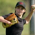 Female baseball pitcher in black shirt throwing a ball with her right hand, glove on left hand on a field.