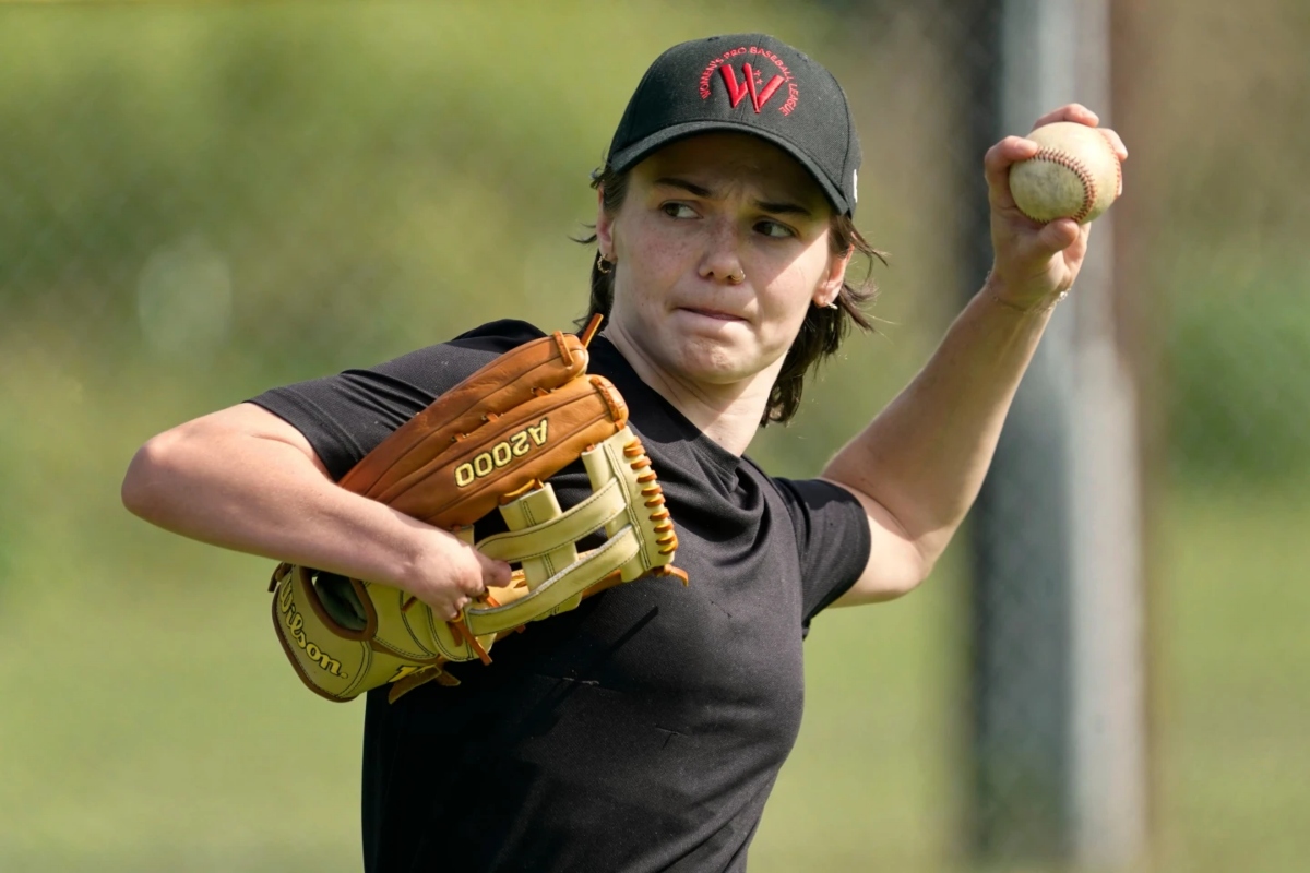 Female baseball pitcher in black shirt throwing a ball with her right hand, glove on left hand on a field.