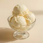 Three scoops of vanilla ice cream in a clear glass dessert bowl on a pale surface.