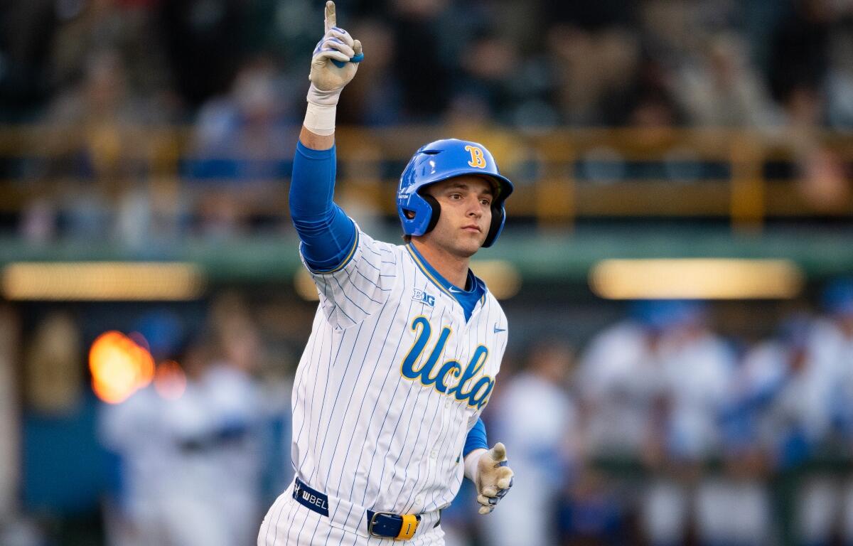 Baseball player in a UCLA pinstriped uniform raises his index finger in celebration on the field.