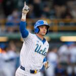 Baseball player in a UCLA pinstriped uniform raises his index finger in celebration on the field.