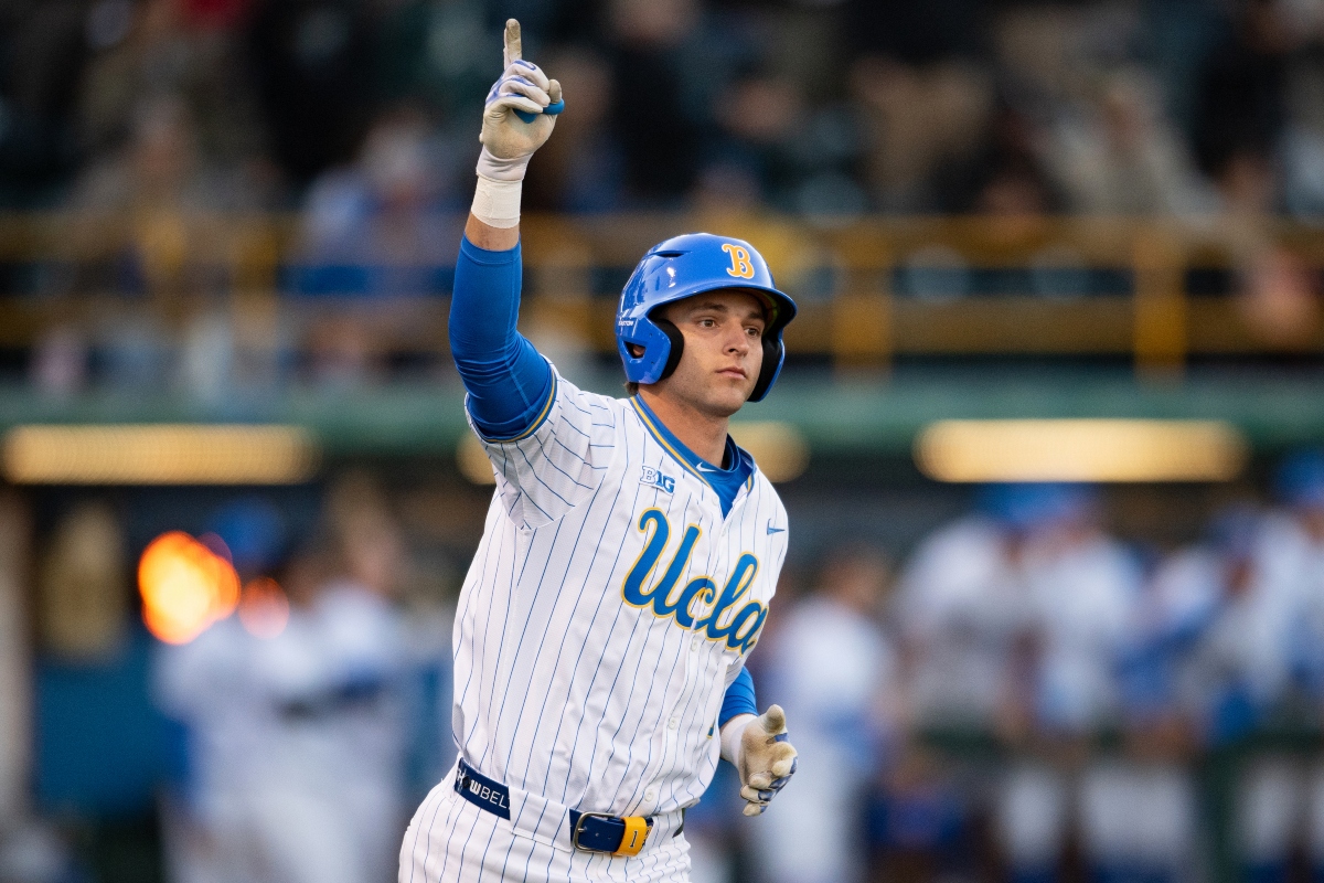 Baseball player in a UCLA pinstriped uniform raises his index finger in celebration on the field.