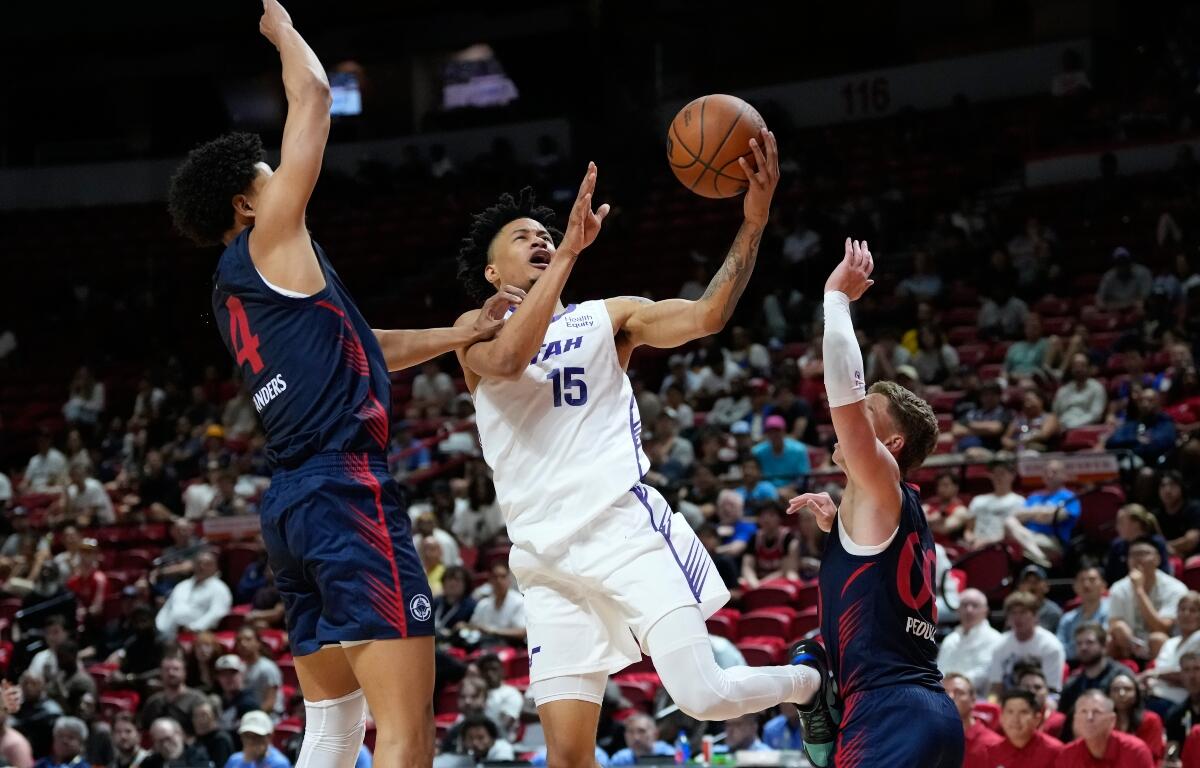 Basketball player in white #15 drives to the hoop while two defenders in blue contest the shot.