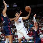 Basketball player in white #15 drives to the hoop while two defenders in blue contest the shot.