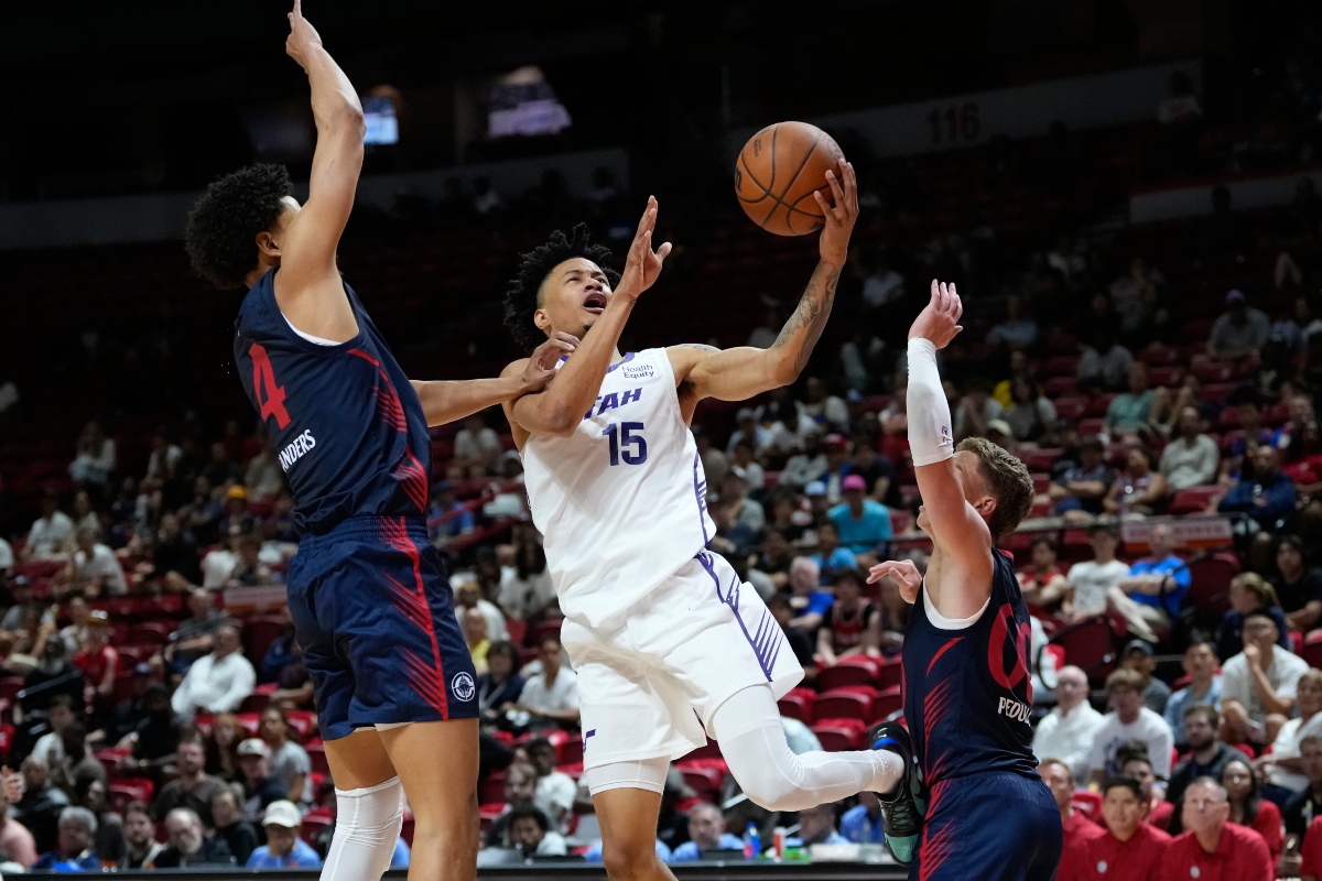 Basketball player in white #15 drives to the hoop while two defenders in blue contest the shot.