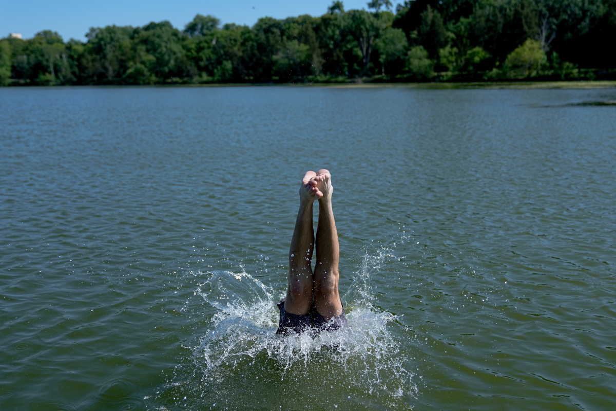 A swimmer dives into Cedar Lake during an extreme heat warning Monday, July 13, 2026, in Minneapolis. (AP Photo/Ellen Schmidt)