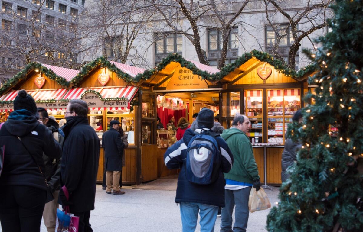 Outdoor Christmas market stalls with striped awnings and shoppers in winter coats at dusk, lit by festive lights.