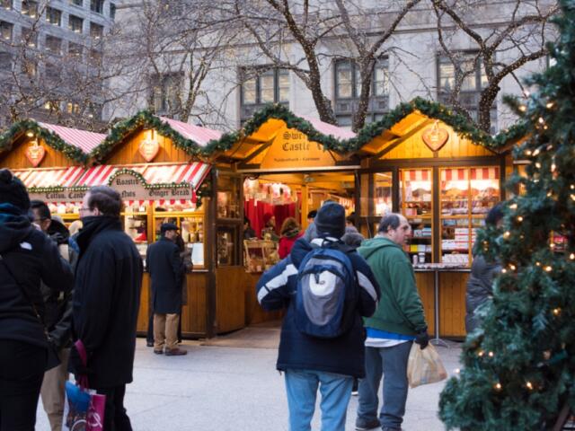 Outdoor Christmas market stalls with striped awnings and shoppers in winter coats at dusk, lit by festive lights.