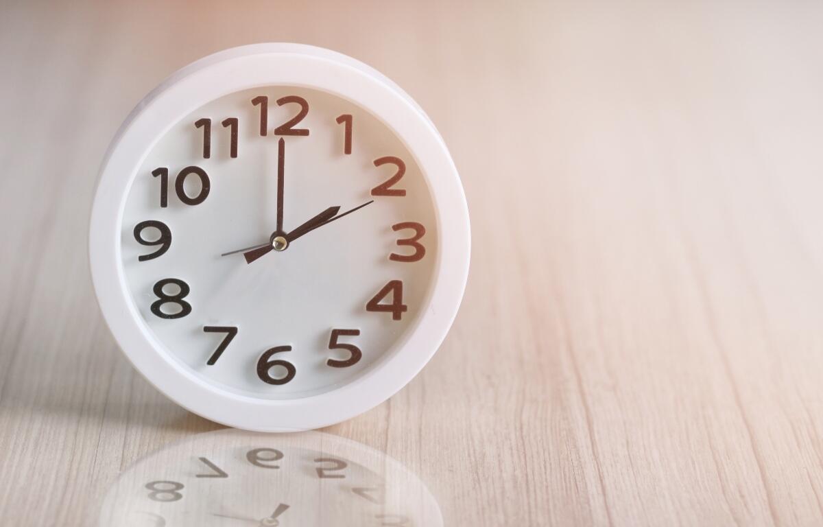White round analog clock on a light wooden surface, showing almost twelve o'clock.