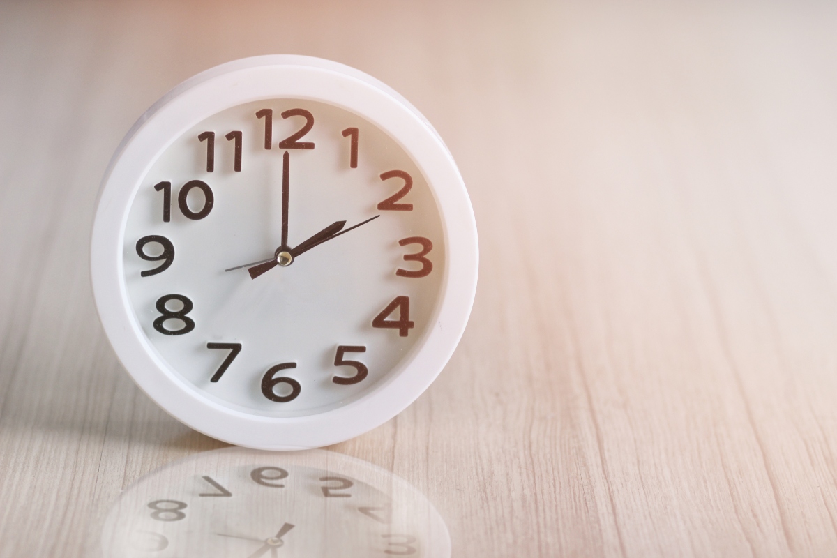 White round analog clock on a light wooden surface, showing almost twelve o'clock.