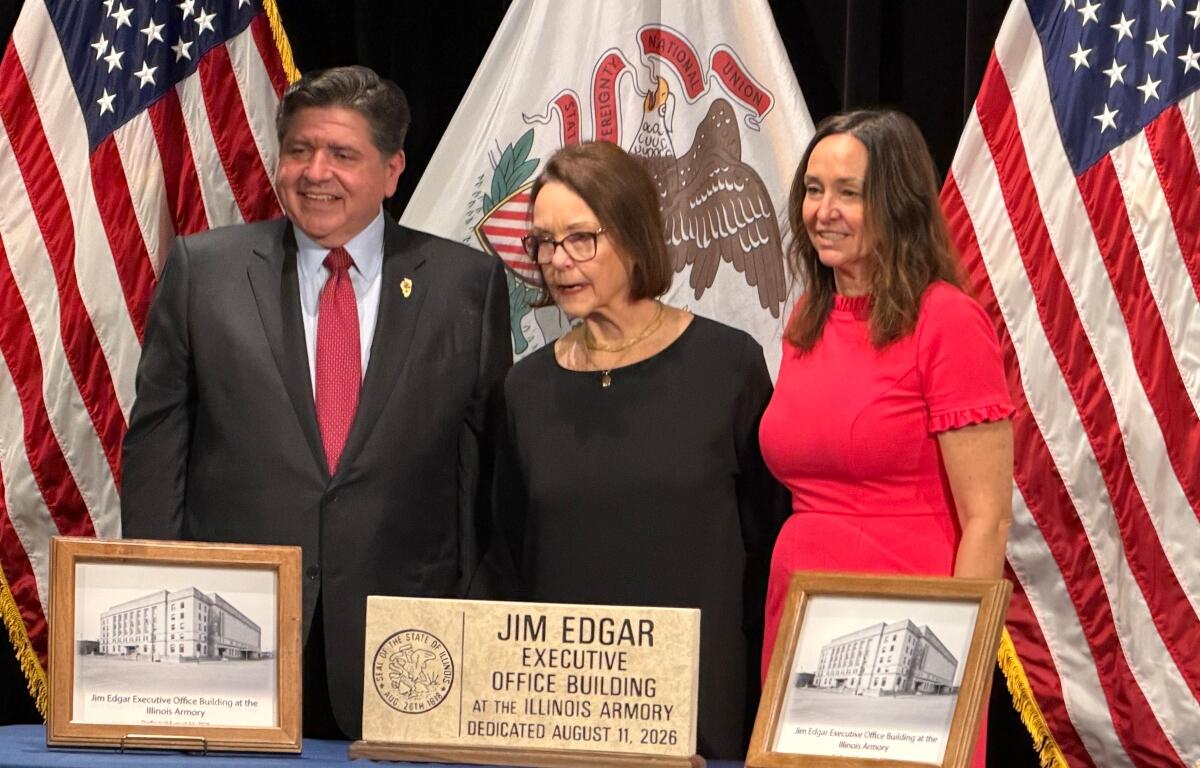 Governor JB Pritzker, widow Brenda Edgar, and daughter Elizabeth, pose in front of plaques and a hand-made sign to be placed at the Illinois Armory, now the Jim Edgar Executive Office Building.