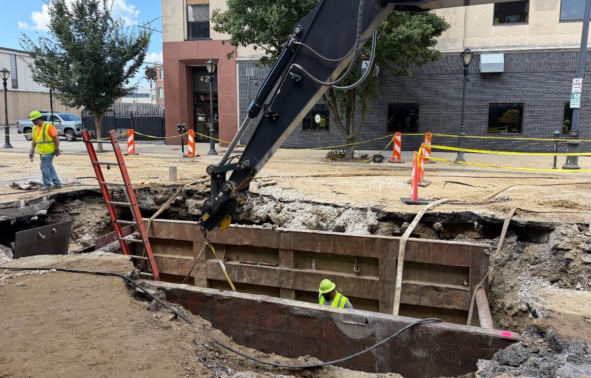 A City Water, Light, and Power employee works in the hole opened up in the road at the site of a water main break, while another employee is in the road.