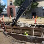 A City Water, Light, and Power employee works in the hole opened up in the road at the site of a water main break, while another employee is in the road.