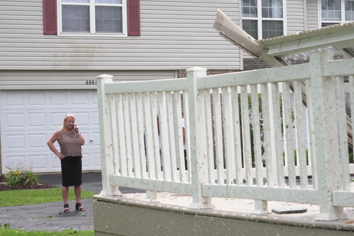 Kerry Hourigan speaks on the phone after reviewing damage a storm caused to her home in Tinley Park, Ill., Tuesday, Aug. 11, 2026. (AP Photo/Laura Bargfeld)