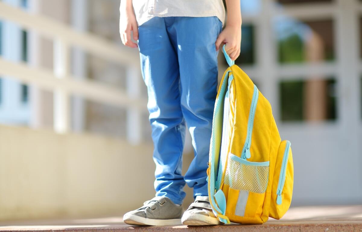 Little student with a backpack on the steps of the stairs of school building. Close-up of child legs, hands and schoolbag of boy standing on staircase of schoolhouse.