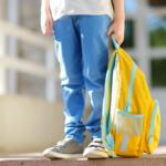 Little student with a backpack on the steps of the stairs of school building. Close-up of child legs, hands and schoolbag of boy standing on staircase of schoolhouse.