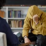 Portrait of distressed teenage boy sharing mental health troubles with therapist while sitting on chair and hiding face during one on one session copy space