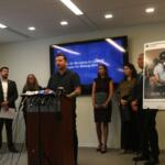 Harvard data scientist Kyle Frankovich stands at a Sept. 17, 2026, news conference between photos of Department of Homeland Security social media posts using images of him with his arms zip-tied behind his back after protesting at the Broadview immigration detention center. (Capitol News Illinois photo by Maggie Dougherty