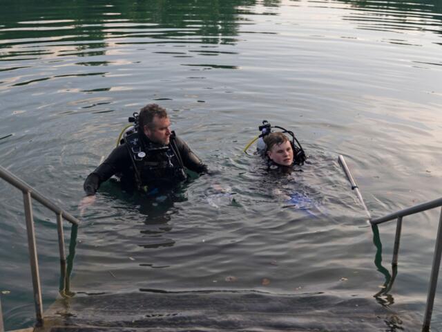 Allen Jones looks toward his son Adrian Jones, who is taking off his fins before stepping out of the Mermet Springs quarry on July 17, 2026, at Mermet Springs in Belknap, Illinois. The father and son got certified together almost a year ago. (Peyton Cook for the Saluki Local Reporting Lab)