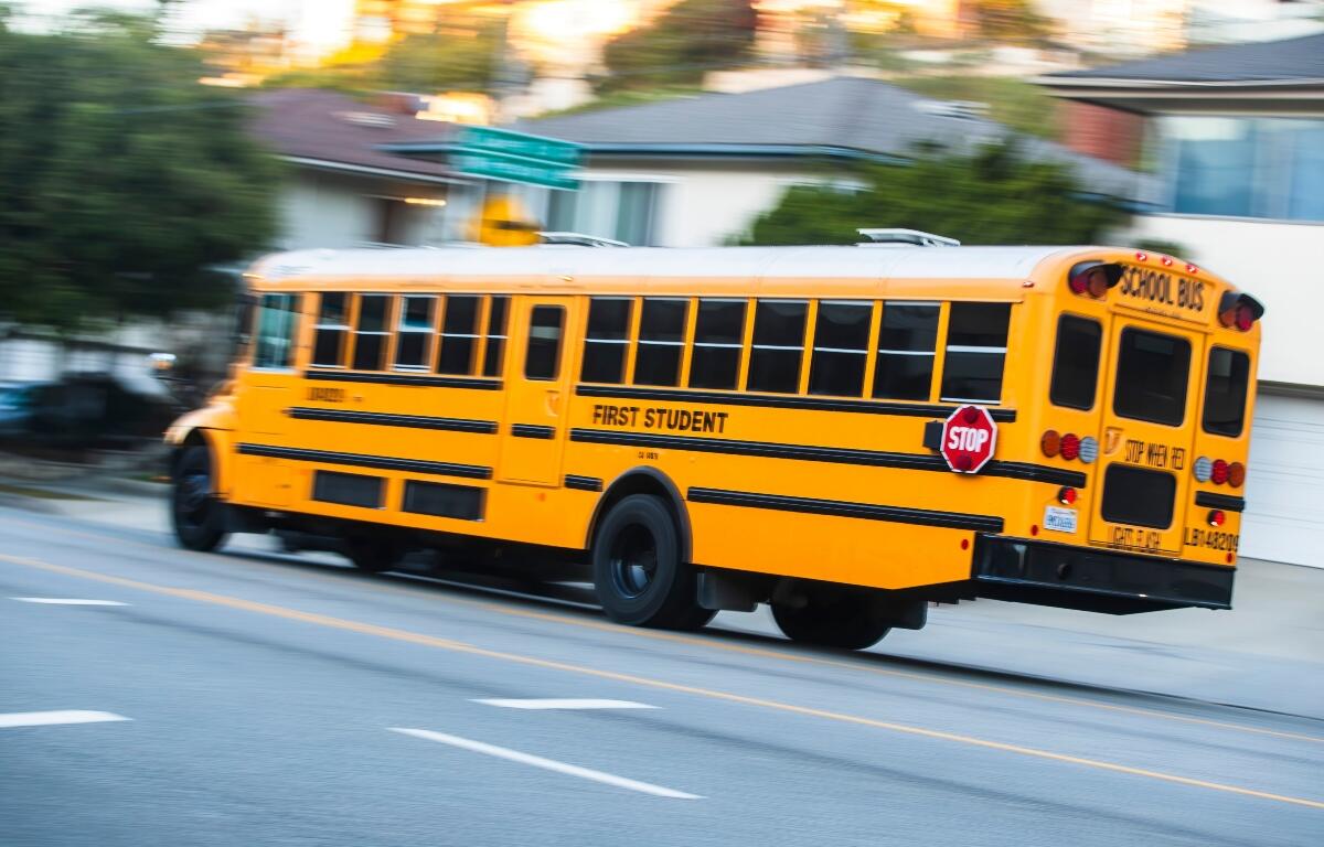2024-11-15 Los Angeles USA Yellow school bus in motion on a city street, with "First Student" branding and a visible "STOP" sign.