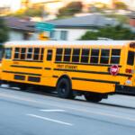 2024-11-15 Los Angeles USA Yellow school bus in motion on a city street, with "First Student" branding and a visible "STOP" sign.