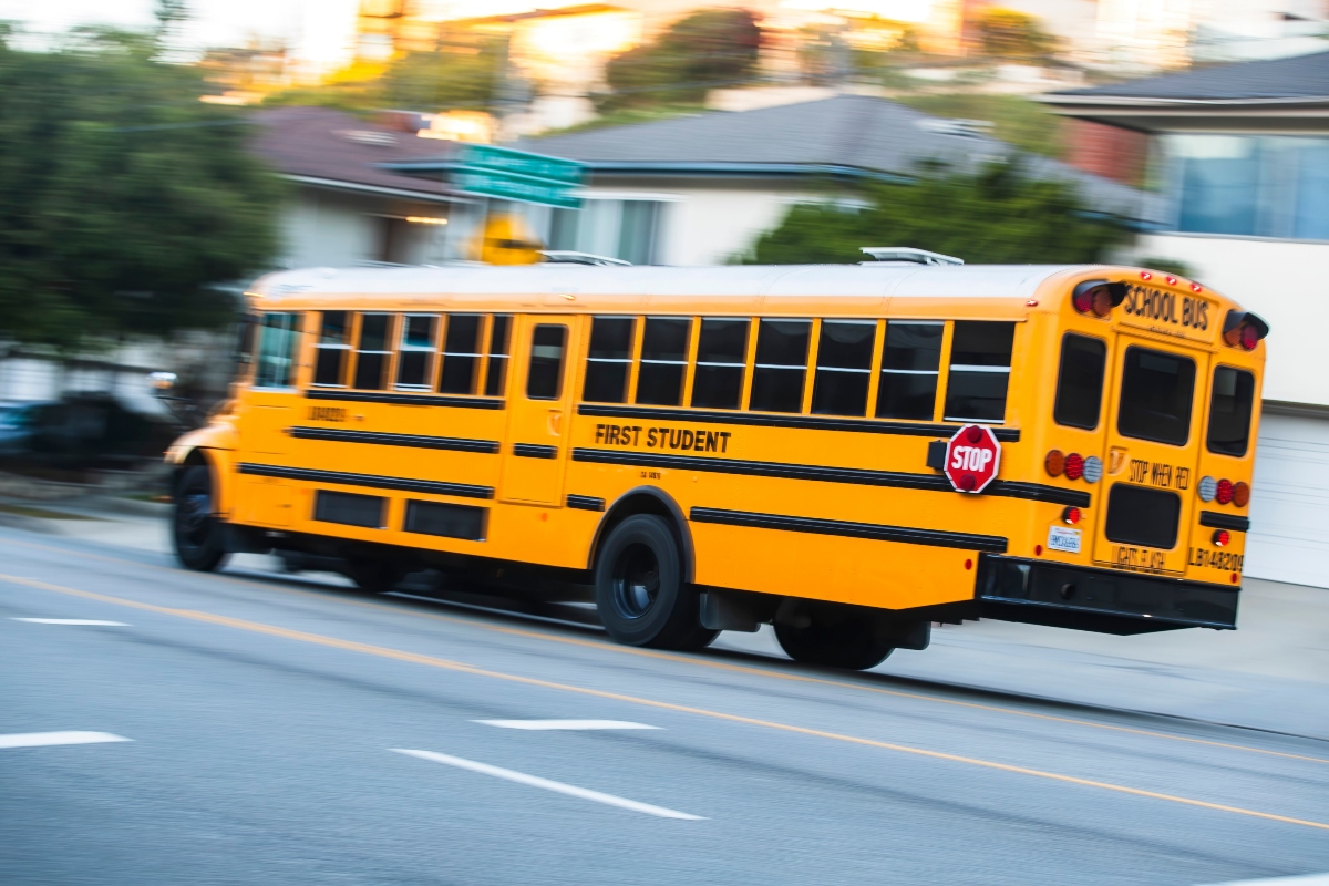 2024-11-15 Los Angeles USA Yellow school bus in motion on a city street, with "First Student" branding and a visible "STOP" sign.