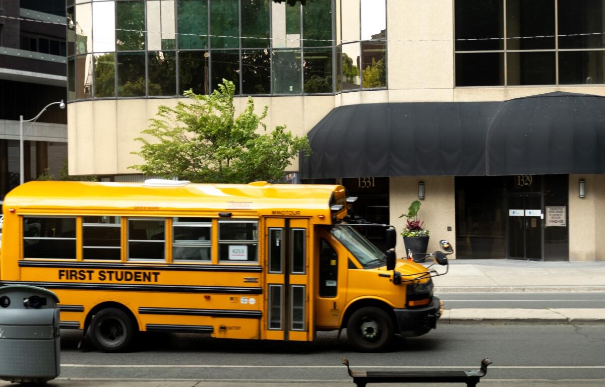 Yellow school bus passes by urban building on a sunny day in the city