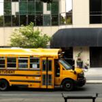 Yellow school bus passes by urban building on a sunny day in the city
