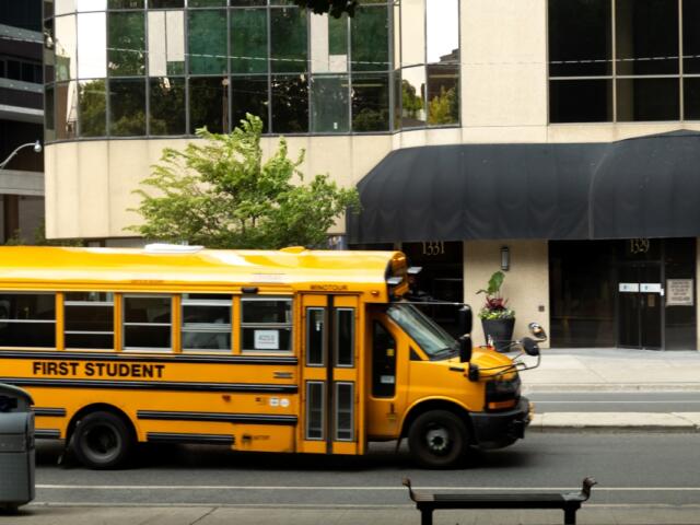 Yellow school bus passes by urban building on a sunny day in the city