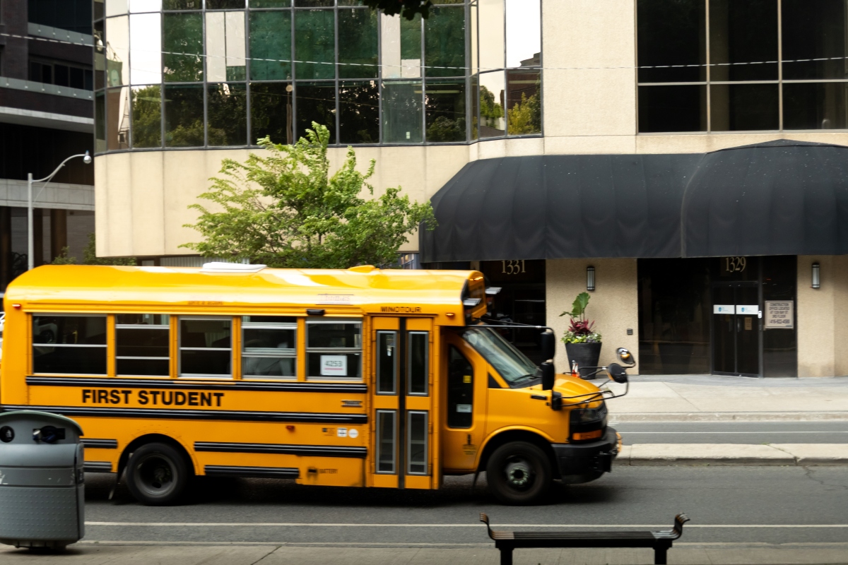 Yellow school bus passes by urban building on a sunny day in the city