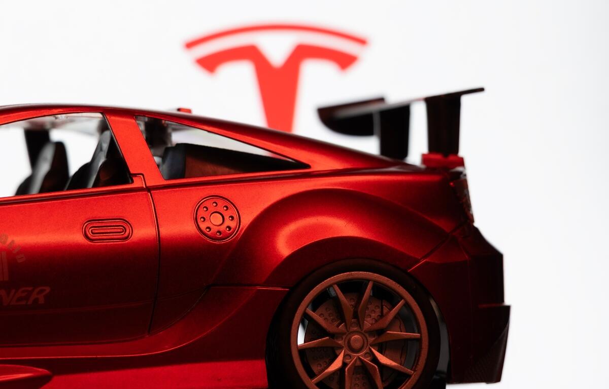 Dhaka, Bangladesh - 10 Aug 2026: A red toy sports car is seen in focus against the Tesla logo on a monitor screen.