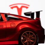 Dhaka, Bangladesh - 10 Aug 2026: A red toy sports car is seen in focus against the Tesla logo on a monitor screen.
