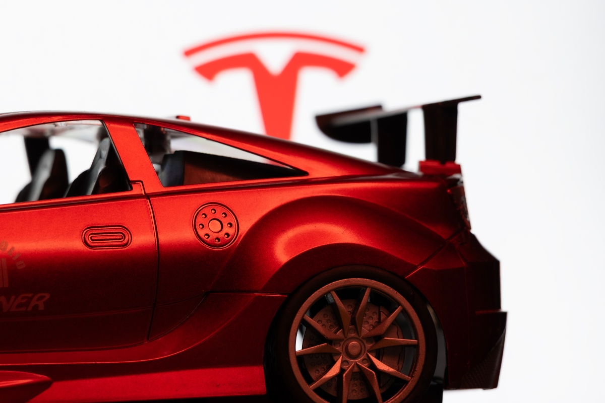 Dhaka, Bangladesh - 10 Aug 2026: A red toy sports car is seen in focus against the Tesla logo on a monitor screen.